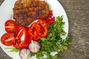 Meat steak cooked on the barbecue. Grilled fresh meat steak with spices and red pepper. Ready steak on the table with tomatoes and peppers. The concept of food, restaurants, traditional cuisine. 