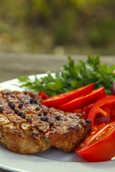 Meat steak cooked on the barbecue. Grilled fresh meat steak with spices and red pepper. Ready steak on the table with tomatoes and peppers. The concept of food, restaurants, traditional cuisine. 