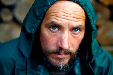 Odun arka planında sakallı bir adamın portresi. Sakallı bir adam ormanda odun kestikten sonra kameraya poz verir. Erkeklik, doğalcılık, hayatta kalma kavramı.. 