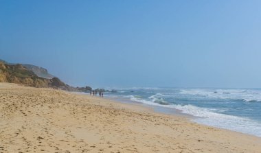 Okyanus kıyısında insanların dinlendiği bir sahil, tatil yeri. Dağlar, deniz ve dalgalar. Avrupa 'ya, Portekiz' e git. Praia de Vale Furado.