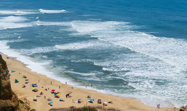 Beach by the ocean with people resting, vacation spot. Mountains, sea and waves. Travel to Europe Portugal. Praia de Vale Furado.