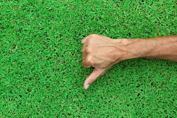 Mão mostrando polegar para baixo na textura de fundo de grama verde — Fotografia de Stock