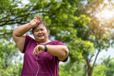 Fat woman asian checking time or heart rate from smart watch. Exercise outdoors for weight loss idea concept 