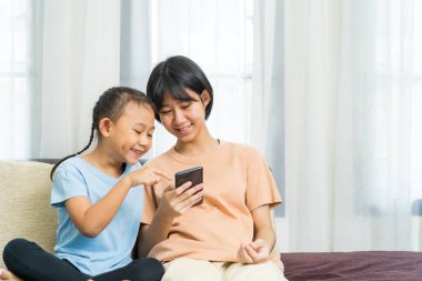 Mutlu Asyalı kız ve kız kardeşi evde akıllı telefonda oynuyorlar.