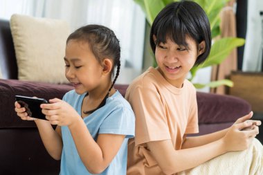 Mutlu Asyalı kız ve kız kardeşi evde akıllı telefonda oynuyorlar.