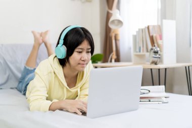 Asyalı kız dizüstü bilgisayar kullanıyor ve evde yatakta yatıyor..