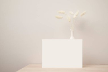 Boş kağıt kart, tebrik kartı maketi. Kurumuş Tavşan Kuyruğu, Ön Manzara, Ahşap masa üzerinde Güzel Tavşan Kuyruğu Çimi ve bej beton arka plan