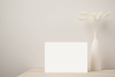 Boş kağıt kart, tebrik kartı maketi. Kurumuş Tavşan Kuyruğu, Ön Manzara, Ahşap masa üzerinde Güzel Tavşan Kuyruğu Çimi ve bej beton arka plan