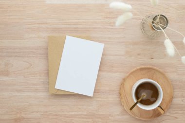 Boş kağıt kartlar, boş tebrik kartı davetiyesi vazoda kurutulmuş tavşan kuyruğu çimeni ahşap masa üzerinde kahve fincanı, ahşap masa arkaplanı, minimum ahşap masa çalışma alanı kompozisyonu, düz yatak, model.