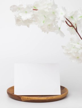 Tebrik kartı maketi. Beyaz çiçekli dekorasyon, ön manzara, tahta tabakta boş kağıt kart ve beyaz arkaplan