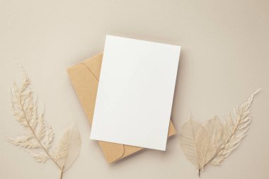 Boş tebrik kartı daveti. Kahverengi zarf üzerinde Mockup 5x7. Bej arka planda kurumuş çiçekler.