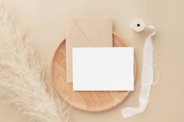 Boş tebrik kartı daveti. Kahverengi zarfın üzerinde bej arka planda otlar, minimum masa iş yeri kompozisyonu, düz yatış, maket modeli.
