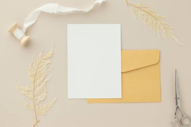 Boş tebrik kartı daveti. Kahverengi zarf üzerinde Mockup 5x7. Bej arka planda kurumuş çiçekler.
