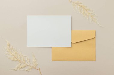 Boş tebrik kartı daveti. Kahverengi zarf üzerinde Mockup 5x7. Bej arka planda kurumuş çiçekler.