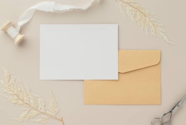Boş tebrik kartı daveti. Kahverengi zarf üzerinde Mockup 5x7. Bej arka planda kurumuş çiçekler.