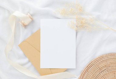 Boş tebrik kartı daveti Kuru çiçekli zarf üzerinde Mockup 5x7 ve beyaz kumaş arka planda kurdele, düz yatış, model