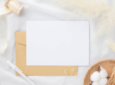 Boş tebrik kartı daveti Kuru çiçekli zarf üzerinde Mockup 5x7 ve beyaz kumaş arka planda kurdele, düz yatış, model