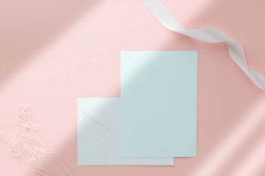 Boş tebrik kartı daveti. Kuru çiçekli zarfın üstüne Mockup 5x7 ve pembe pastel arka planda kurdele.