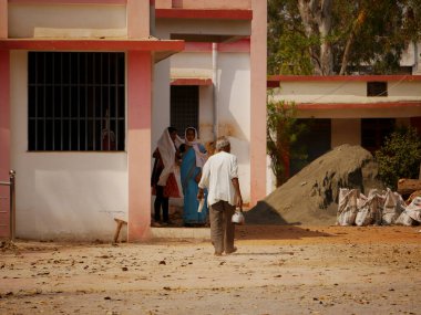 Hindistan 'da fakir bir adam çaydanlıkla gündüz bina yapmaya giderken, Hindistan' da Katni Madhya Pradesh şehrinde kadınlar arka planda 2022 Mart 'ında.