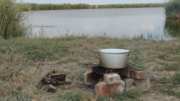 На вогнищі на березі річки варений рибний суп — стокове відео