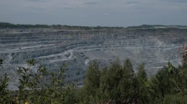 Asbest ocağı, açık çukurda çalışan bir çöp kamyonu. Çöp kamyonları, maden endüstrisi, maden kamyonları, yük treni. Açık maden ocağının havadan çekilmiş videosu. Bir sürü makine çalışıyor..