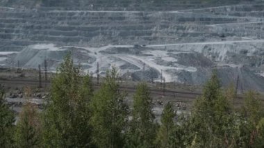 Asbest ocağı, açık çukurda çalışan bir çöp kamyonu. Çöp kamyonları, maden endüstrisi, maden kamyonları, yük treni. Açık maden ocağının havadan çekilmiş videosu. Bir sürü makine çalışıyor..