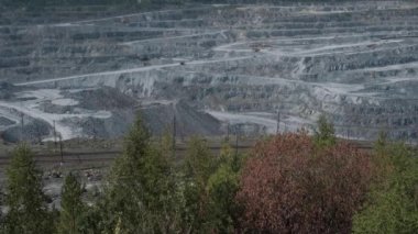 Asbest ocağı, açık çukurda çalışan bir çöp kamyonu. Çöp kamyonları, maden endüstrisi, maden kamyonları, yük treni. Açık maden ocağının havadan çekilmiş videosu. Bir sürü makine çalışıyor..