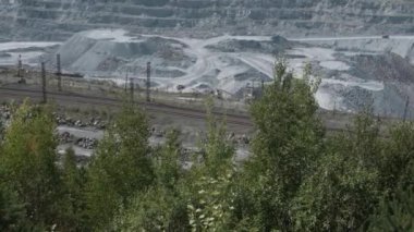 Asbest ocağı, açık çukurda çalışan bir çöp kamyonu. Çöp kamyonları, maden endüstrisi, maden kamyonları, yük treni. Açık maden ocağının havadan çekilmiş videosu. Bir sürü makine çalışıyor..