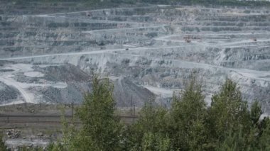 Asbest ocağı, açık çukurda çalışan bir çöp kamyonu. Çöp kamyonları, maden endüstrisi, maden kamyonları, yük treni. Açık maden ocağının havadan çekilmiş videosu. Bir sürü makine çalışıyor..