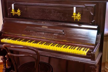 Beautiful old wooden piano and black finishes along with a spotlight that illuminates its design. Retro piano, classic style. Instrumental classical music. Classic culture. Vintage, retro, obsolete.