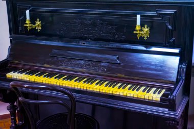Beautiful old wooden piano and black finishes along with a spotlight that illuminates its design. Retro piano, classic style. Instrumental classical music. Classic culture. Vintage, retro, obsolete.