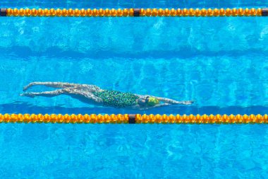 Yüzen kız sporcu, sarı havuz şeridi işaretleri arasında su altında tanınmaz halde yüzme tekmesi atıyor. Başlığın üstünde eylem fotoğrafı .