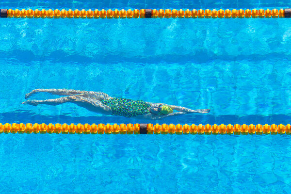 Swimming girl athlete training unrecognizable underwater backstroke kick between yellow pool lane markers . Action photo overhead .