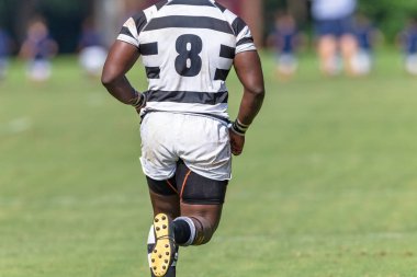 Rugby oyuncusu oyun sahasında başsız koşuyor. Yakın plan, 8 numaralı formayla tanınmayan bir sporcunun arkasında..