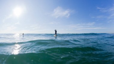 Sörfçü sup kürekçisi tanımlanamayan sörf tahtası üzerinde duran mavi ufukta su fotoğrafının arkasında.
