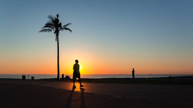 Dawn beach promenade path people silhouetted at sunrise from the horizon ocean  landscape.