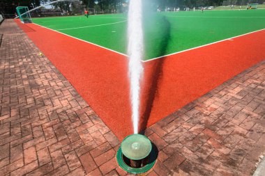 Hockey astro turf field been water sprayed with high powered sprinklers on each side of pitch sports arena.