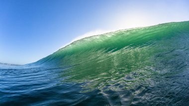 Ocean wave Swimming encounter close-up wall of sea water crashing morning backlit blue sky landscape.