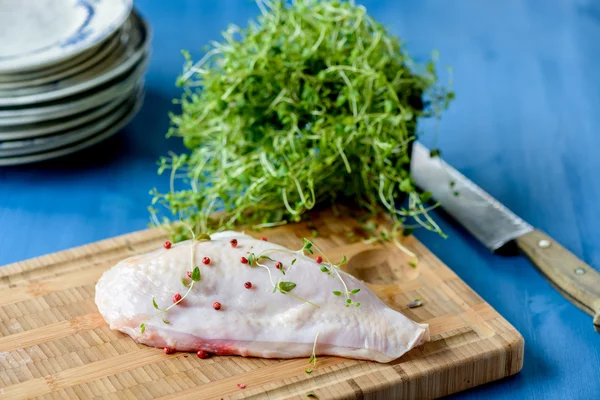 Rohe Hühnerbrust mit noch angesetzter Haut und ein paar Kräutern in der — Stockfoto