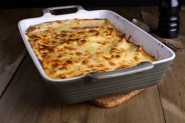 Lasaña en un plato de servir con queso encima en una lengüeta de madera vieja — Foto de Stock