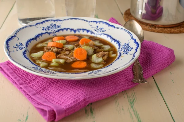 Куриный суп на старинном столе с морковью и сельдереем сверху — стоковое фото