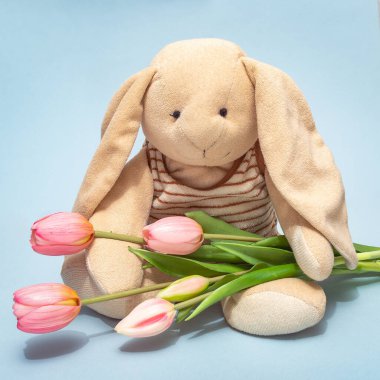 A plush toy rabbit holding a bouquet of pink tulips