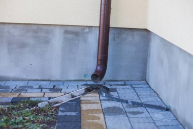 Kenardan gelen suyla yağmur oluğu aşağı akıyor. Taş kiremitlerin etrafında