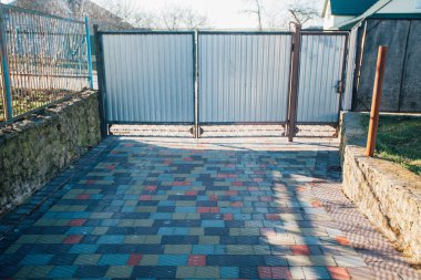Iron gates and fence near the road from paving slabs