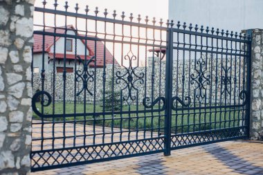 Iron gates and fence near the road from paving slabs