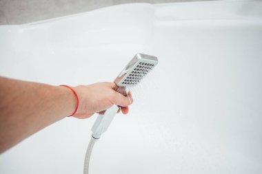 Erkek el banyoda beyaz duvara karşı duş alıyor, yakın çekim. 