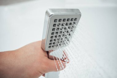 Erkek el banyoda beyaz duvara karşı duş alıyor, yakın çekim. 