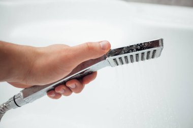 Erkek el banyoda beyaz duvara karşı duş alıyor, yakın çekim. 