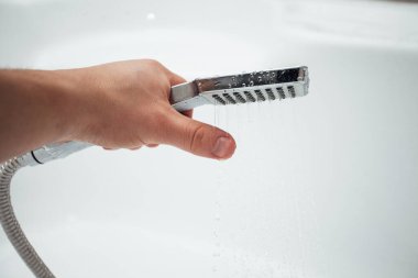 Erkek el banyoda beyaz duvara karşı duş alıyor, yakın çekim. 