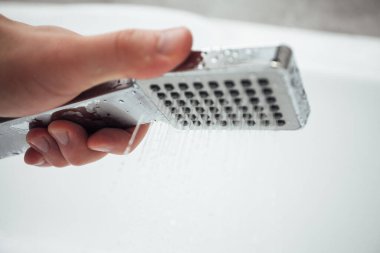 Erkek el banyoda beyaz duvara karşı duş alıyor, yakın çekim. 